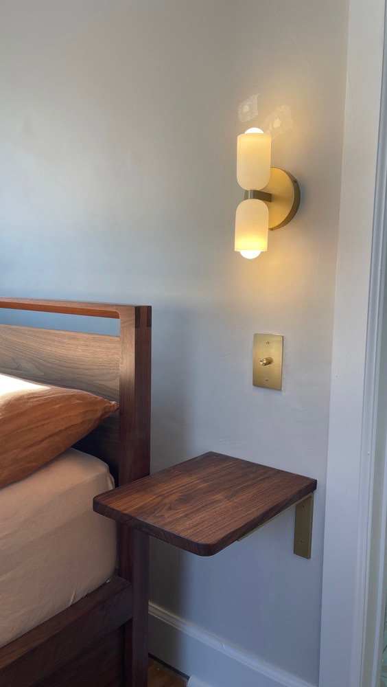 Brass double wall sconce with a matching rotary dimmer beside a bed